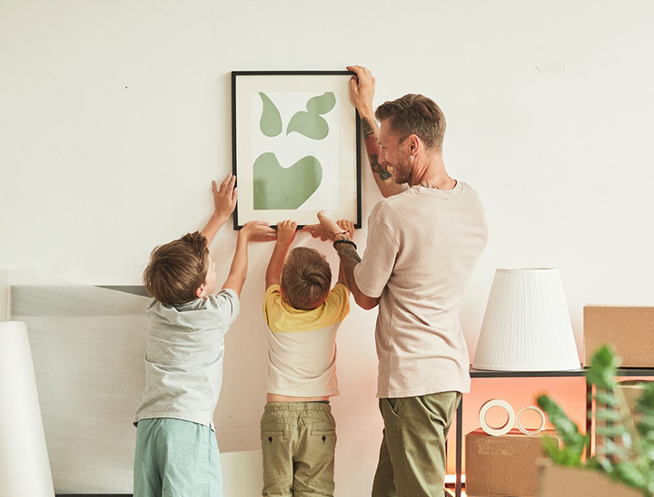 A parent putting up a picture on a wall with help from their children